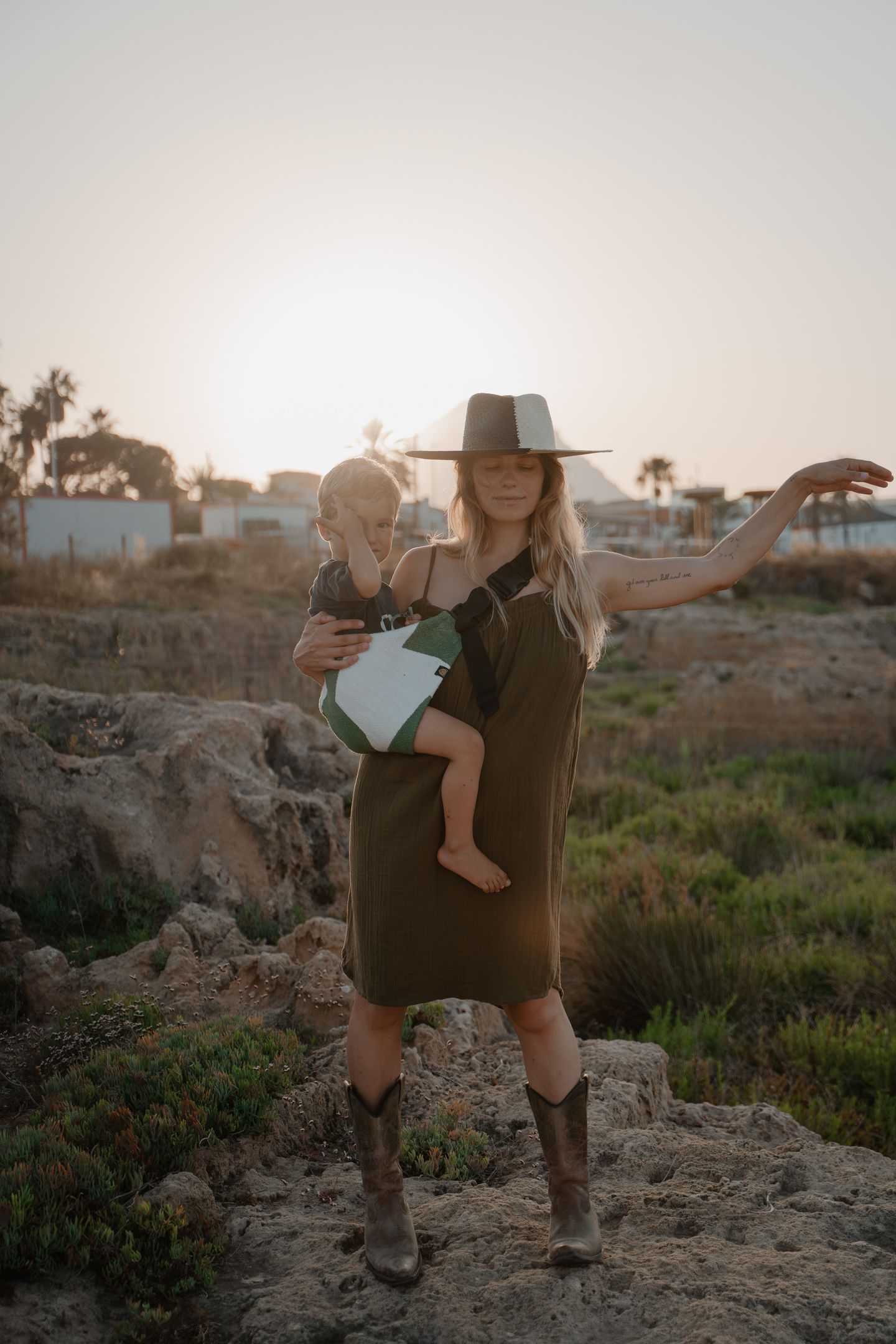 Mother wearing a wide-brim hat holds her toddler in a Wildride hip carrier at sunset. A lightweight, ergonomic toddler carrier designed for comfort and freedom — ideal for parents seeking the best baby carrier for everyday use.