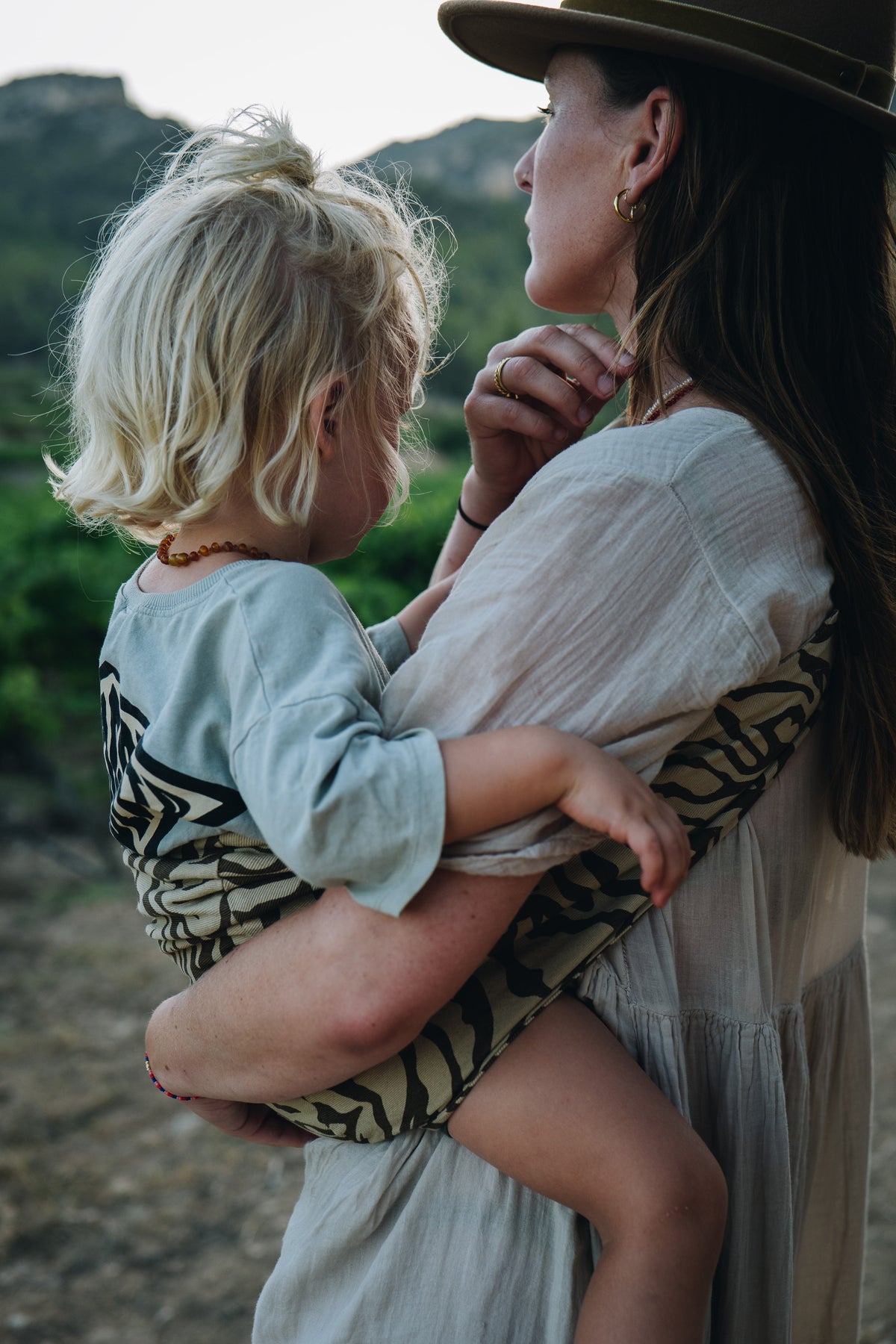 A close moment between mother and child, captured outdoors. The child is carried in a zebra-print Wildride hip carrier as they share a quiet look together.