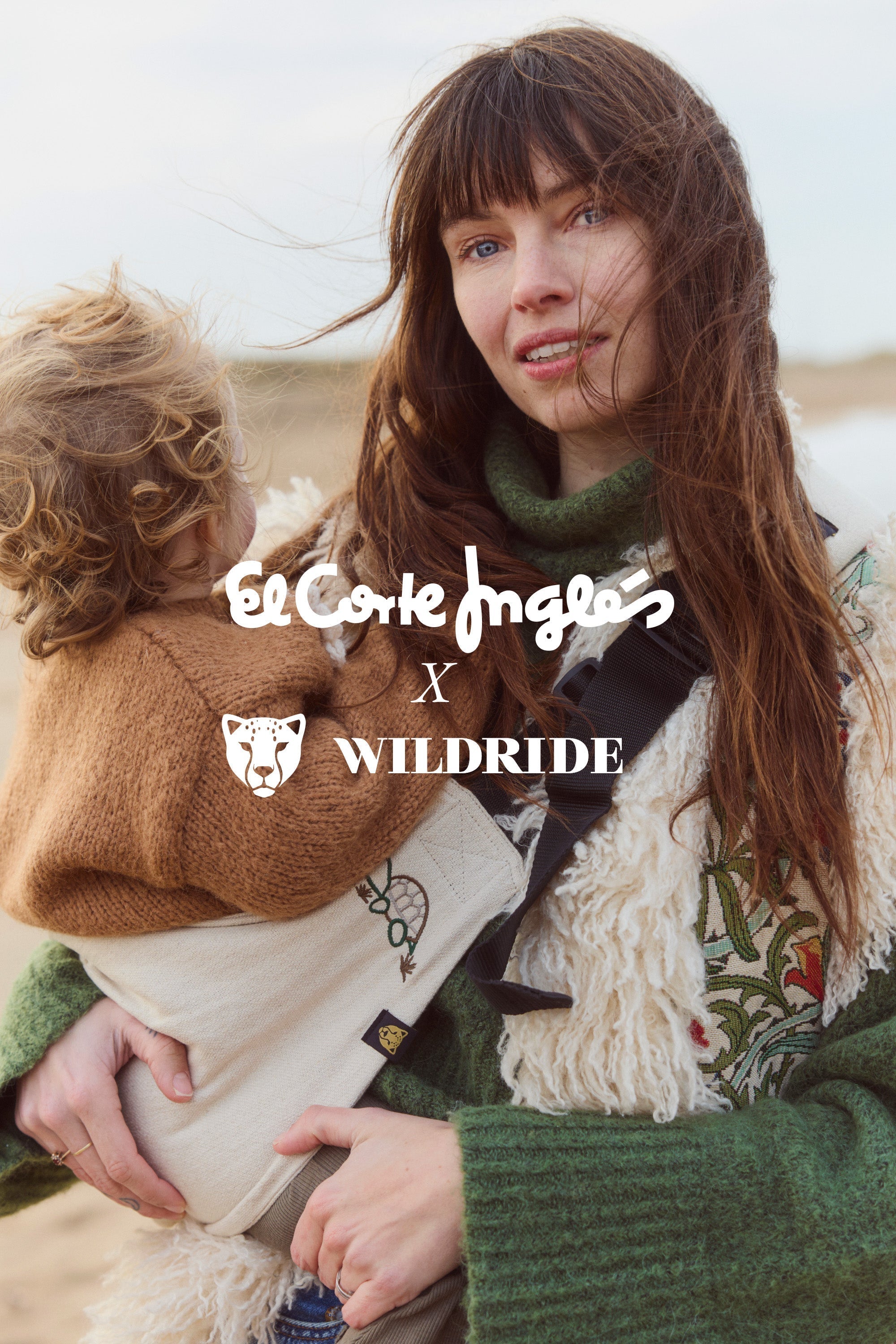 A close-up of a mother holding her toddler in the exclusive Wildride toddler carrier with turtle embroidery, created in collaboration with El Corte Inglés. The image features both brand logos in the center.