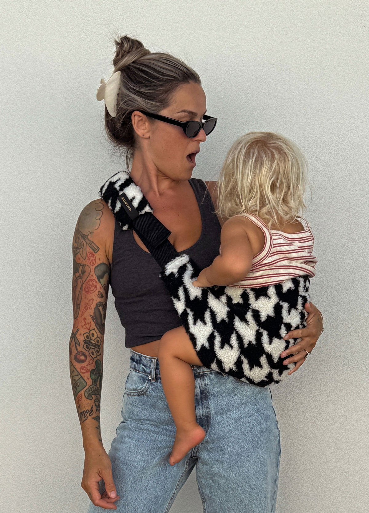 wildride houndstooth teddy toddler carrier — mom carrying child on hip against white wall