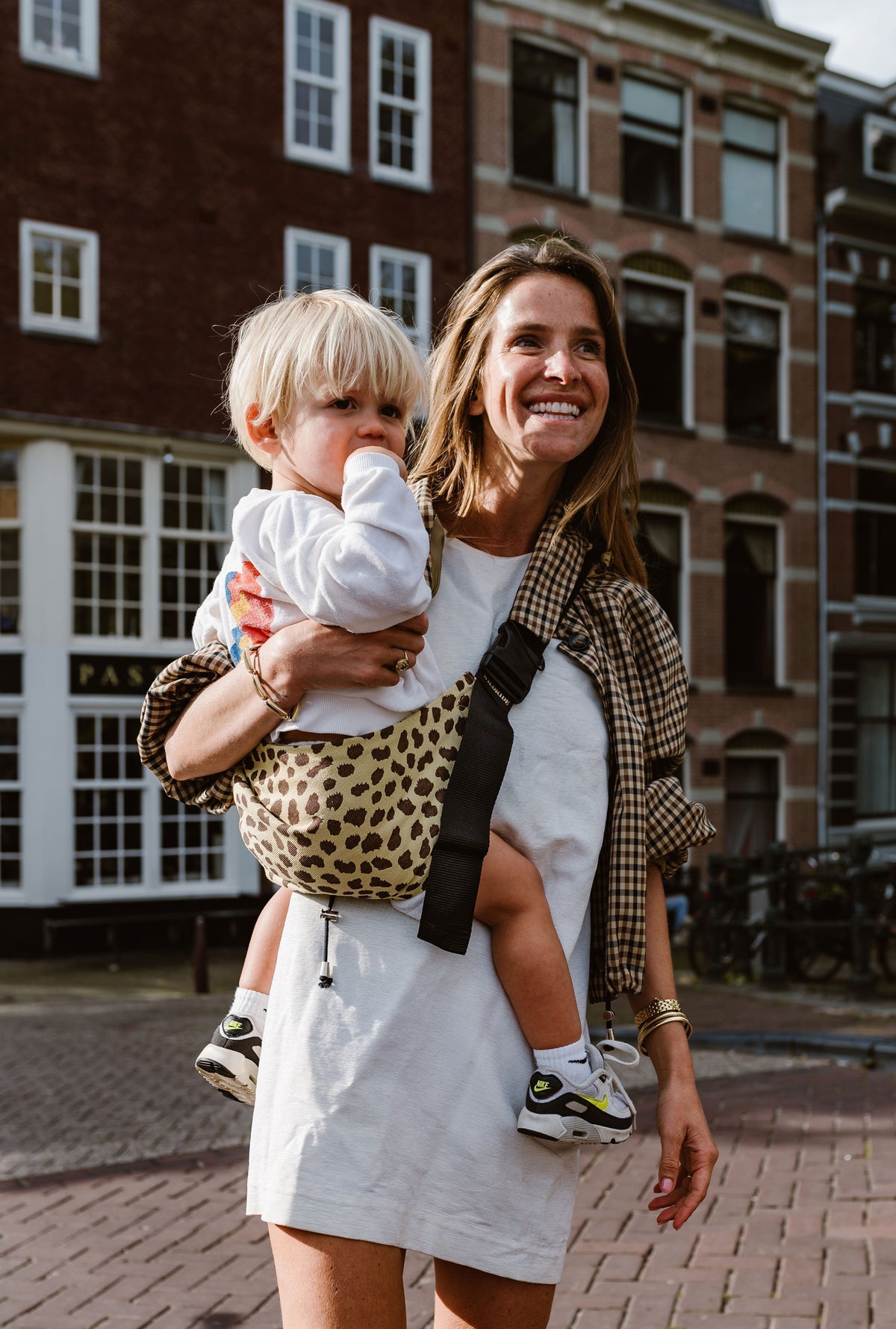 Wildride toddler carrier cheetah print, mom walking with child on hip on a city street