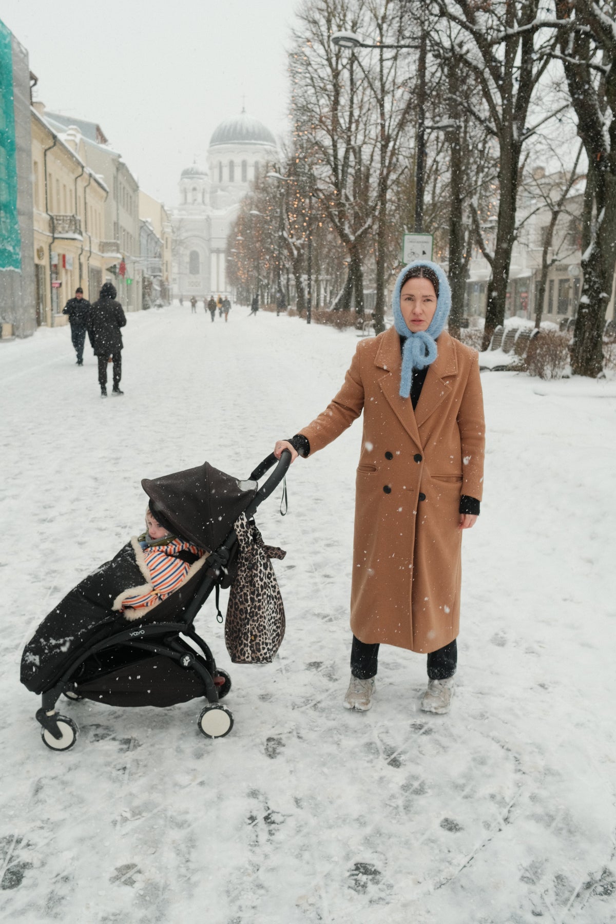 Parent walking with a stroller through a snowy European city in winter